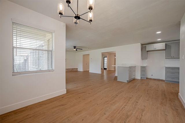 unfurnished living room with ceiling fan with notable chandelier and light hardwood / wood-style flooring