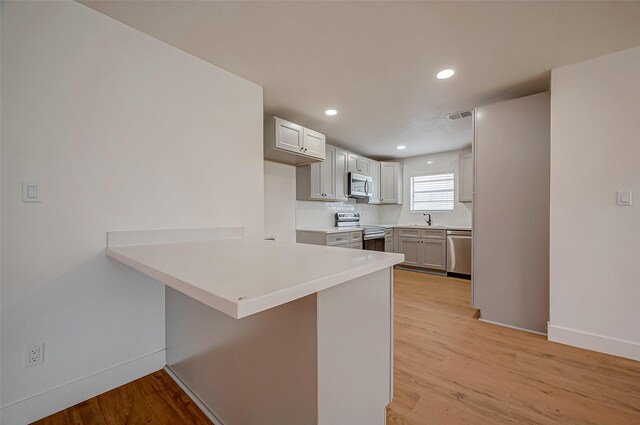 kitchen featuring sink, light wood-type flooring, appliances with stainless steel finishes, a kitchen bar, and kitchen peninsula