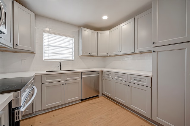 kitchen with gray cabinetry, decorative backsplash, light wood-type flooring, and appliances with stainless steel finishes