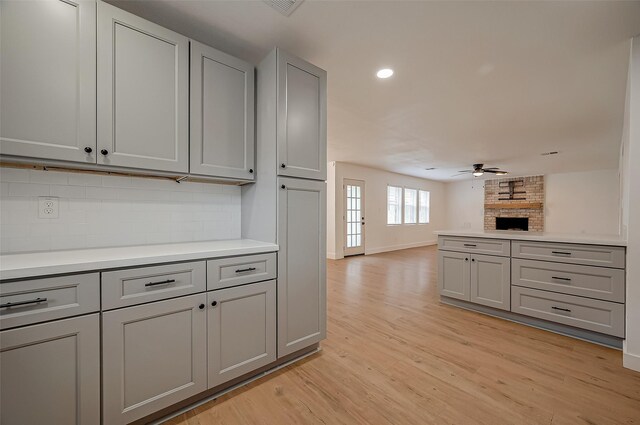 kitchen featuring backsplash, ceiling fan, light hardwood / wood-style flooring, a fireplace, and gray cabinets