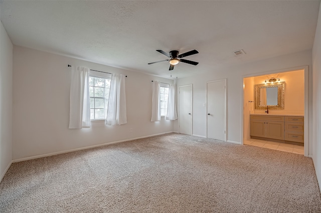 unfurnished bedroom with light colored carpet, ceiling fan, sink, connected bathroom, and multiple closets