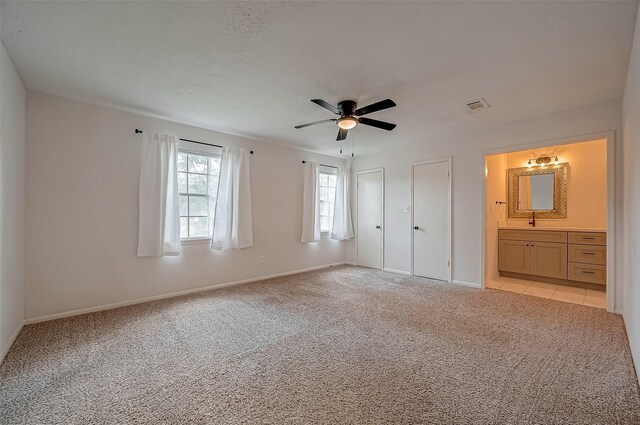 unfurnished bedroom featuring ensuite bathroom, sink, light colored carpet, ceiling fan, and multiple closets