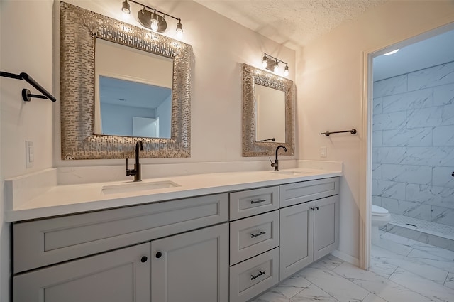 bathroom with vanity, toilet, tiled shower, and a textured ceiling