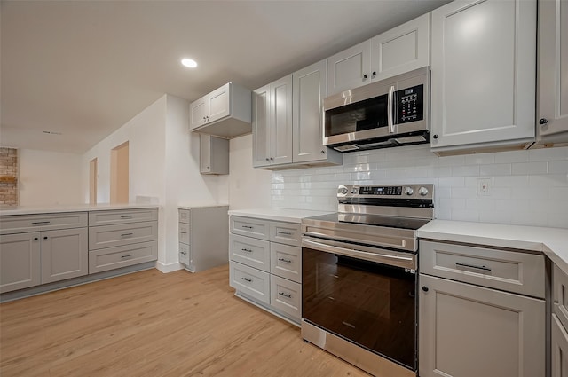 kitchen with gray cabinets, tasteful backsplash, appliances with stainless steel finishes, and light hardwood / wood-style flooring