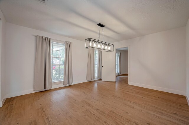 unfurnished dining area with a textured ceiling and light wood-type flooring