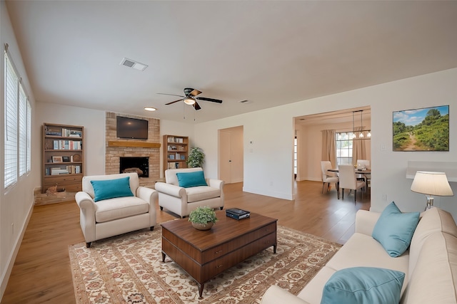 living room featuring hardwood / wood-style floors, ceiling fan with notable chandelier, and a brick fireplace