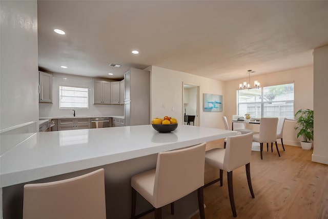 kitchen featuring a kitchen breakfast bar, a notable chandelier, kitchen peninsula, pendant lighting, and light wood-type flooring