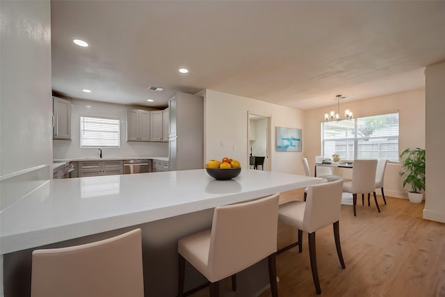 kitchen with a kitchen bar, sink, decorative light fixtures, stainless steel dishwasher, and kitchen peninsula