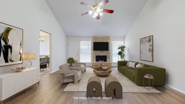 living room featuring a stone fireplace, hardwood / wood-style floors, high vaulted ceiling, and ceiling fan with notable chandelier