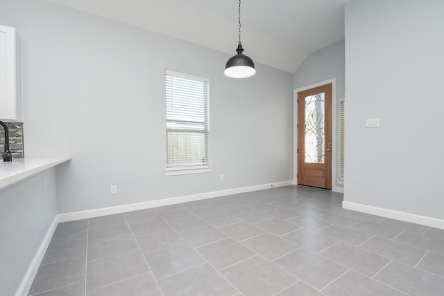 unfurnished dining area with light tile patterned floors, lofted ceiling, and baseboards
