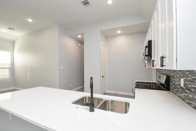 kitchen with kitchen peninsula, stainless steel gas range, sink, white cabinetry, and tasteful backsplash