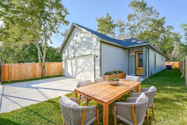 back of house featuring driveway, a lawn, central air condition unit, fence, and a garage