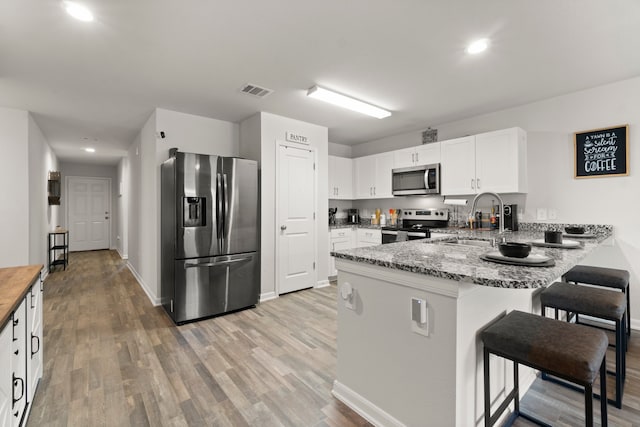 kitchen with light wood-type flooring, white cabinetry, kitchen peninsula, stainless steel appliances, and light stone countertops