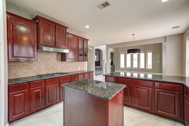 kitchen featuring hanging light fixtures, decorative backsplash, dark stone countertops, stainless steel gas cooktop, and a center island