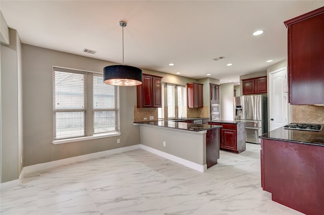 kitchen with kitchen peninsula, decorative light fixtures, appliances with stainless steel finishes, dark stone countertops, and decorative backsplash