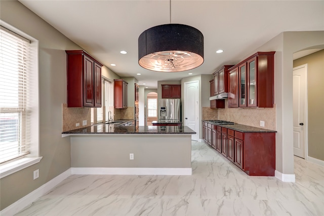 kitchen with appliances with stainless steel finishes, hanging light fixtures, decorative backsplash, kitchen peninsula, and a healthy amount of sunlight