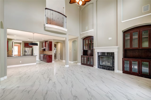 unfurnished living room with a towering ceiling, a high end fireplace, and ceiling fan