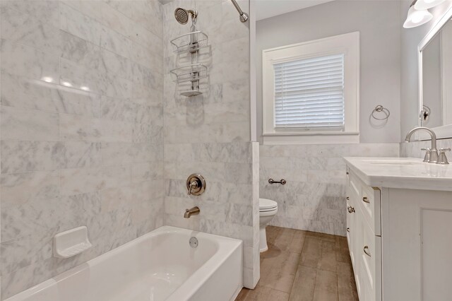 full bathroom with vanity, tiled shower / bath combo, toilet, and tile walls