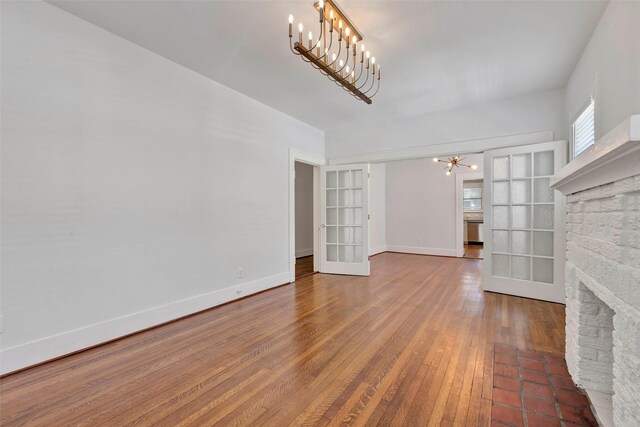 unfurnished living room featuring a notable chandelier, dark hardwood / wood-style flooring, a fireplace, and french doors