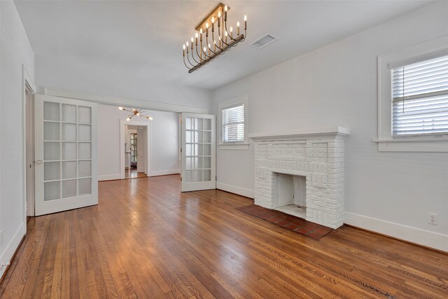 unfurnished living room featuring a chandelier, french doors, wood-type flooring, and a brick fireplace