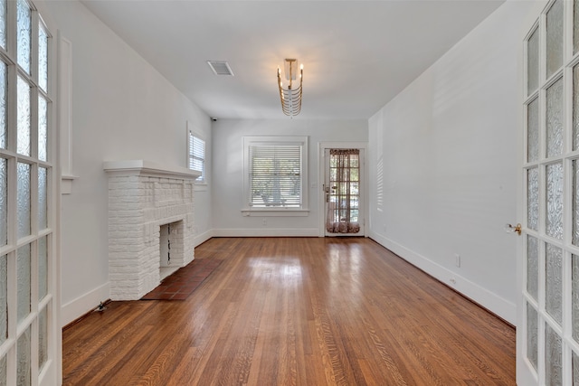 unfurnished living room with french doors, plenty of natural light, dark hardwood / wood-style floors, and a brick fireplace