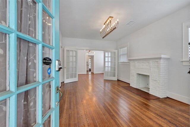 unfurnished living room with a chandelier, french doors, dark wood-type flooring, and a brick fireplace