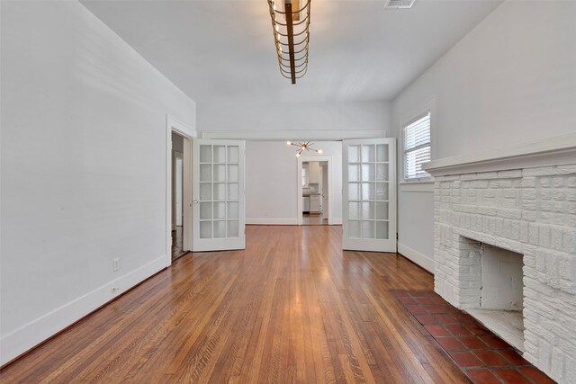 unfurnished living room with a brick fireplace, an inviting chandelier, french doors, and dark wood-type flooring