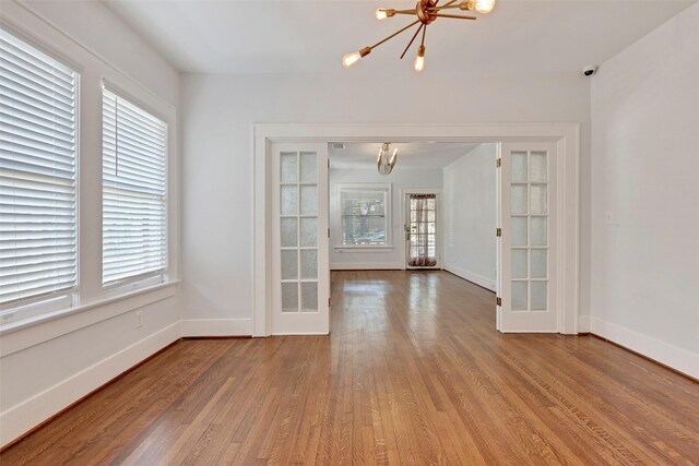 empty room with french doors, light wood-type flooring, and an inviting chandelier