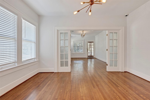 spare room with french doors, a chandelier, and light hardwood / wood-style floors