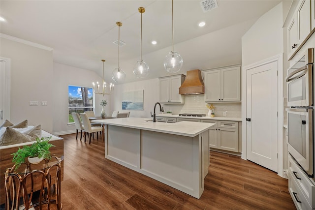 kitchen featuring premium range hood, sink, a center island with sink, hanging light fixtures, and white cabinets