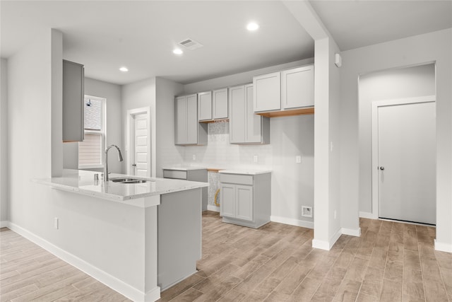 kitchen with gray cabinetry, sink, light hardwood / wood-style flooring, and kitchen peninsula