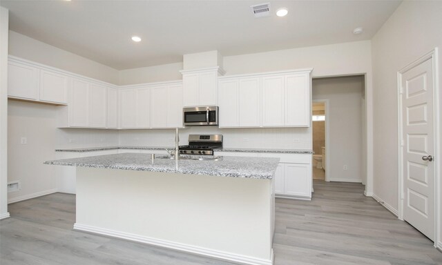 kitchen featuring light wood-type flooring, white cabinetry, a center island with sink, and appliances with stainless steel finishes