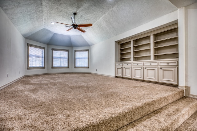 unfurnished living room with a textured ceiling, vaulted ceiling, built in shelves, carpet, and ceiling fan