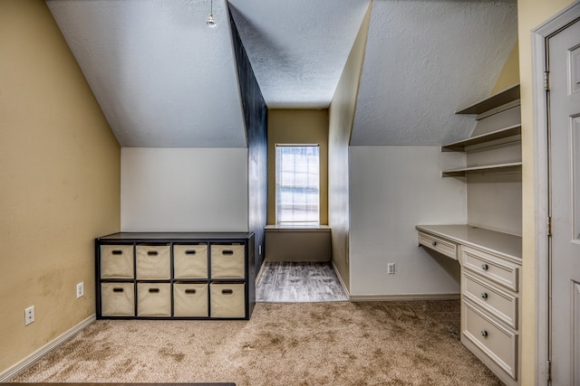 bonus room with built in desk, a textured ceiling, vaulted ceiling, and light carpet