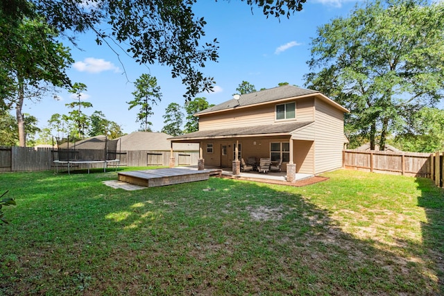 rear view of property with a lawn, a wooden deck, a trampoline, and a patio