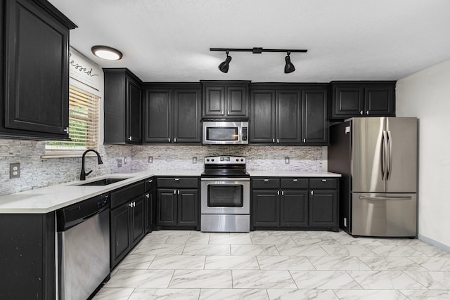 kitchen with appliances with stainless steel finishes, rail lighting, decorative backsplash, a textured ceiling, and sink