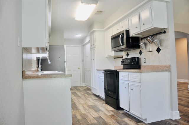 kitchen with light hardwood / wood-style floors, tasteful backsplash, sink, white cabinetry, and black electric range oven