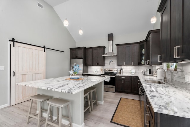 kitchen featuring appliances with stainless steel finishes, high vaulted ceiling, a barn door, a center island, and sink