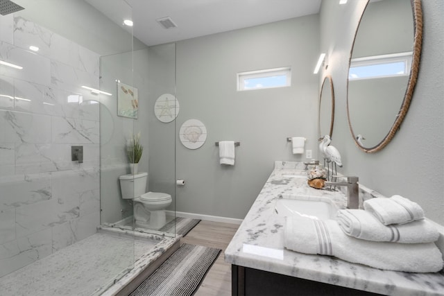 bathroom with wood-type flooring, vanity, a tile shower, and toilet