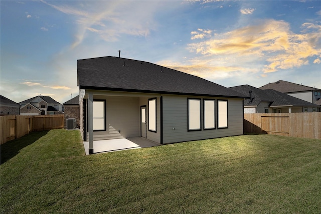 back of property featuring a shingled roof, a lawn, a patio area, cooling unit, and a fenced backyard