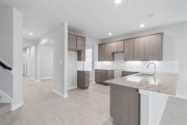 kitchen featuring visible vents, light stone counters, a peninsula, a sink, and backsplash