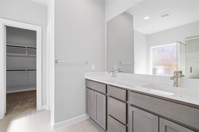 full bath featuring double vanity, a stall shower, visible vents, a walk in closet, and a sink