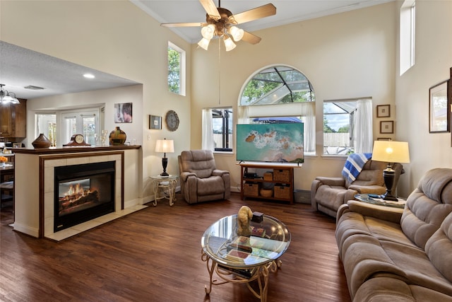 living room featuring a textured ceiling, a tile fireplace, a towering ceiling, dark hardwood / wood-style flooring, and ceiling fan