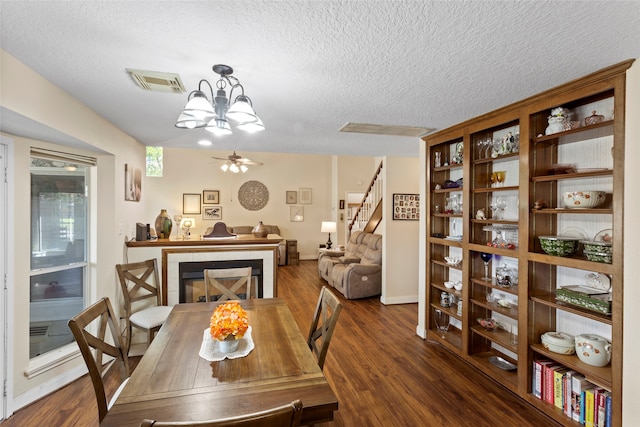 dining room with ceiling fan with notable chandelier, a textured ceiling, a fireplace, and dark hardwood / wood-style floors