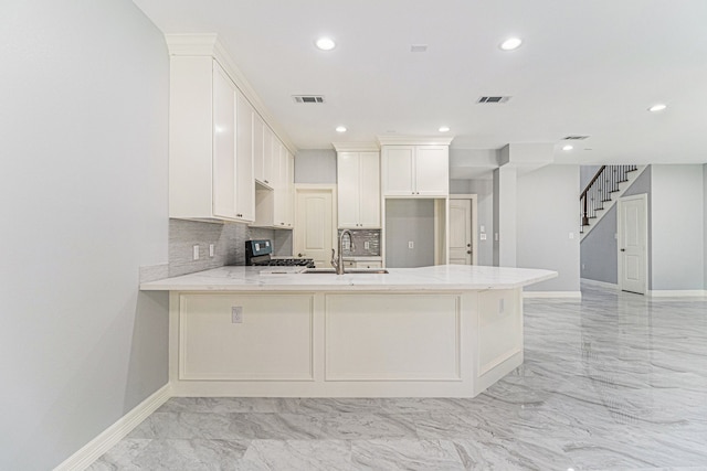 kitchen featuring backsplash, kitchen peninsula, sink, stainless steel range, and white cabinetry