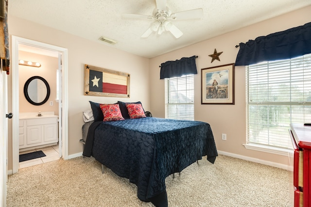 carpeted bedroom featuring ceiling fan, a textured ceiling, ensuite bathroom, and multiple windows