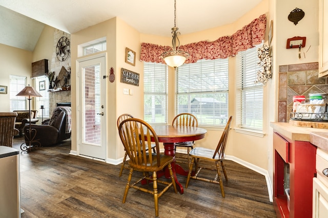 dining space with a stone fireplace, lofted ceiling, dark wood-type flooring, and a wealth of natural light