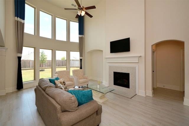 living room featuring light hardwood / wood-style flooring, a high ceiling, ceiling fan, and a fireplace