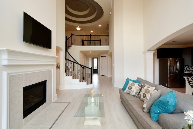 unfurnished living room featuring light wood-type flooring, a tile fireplace, and a towering ceiling