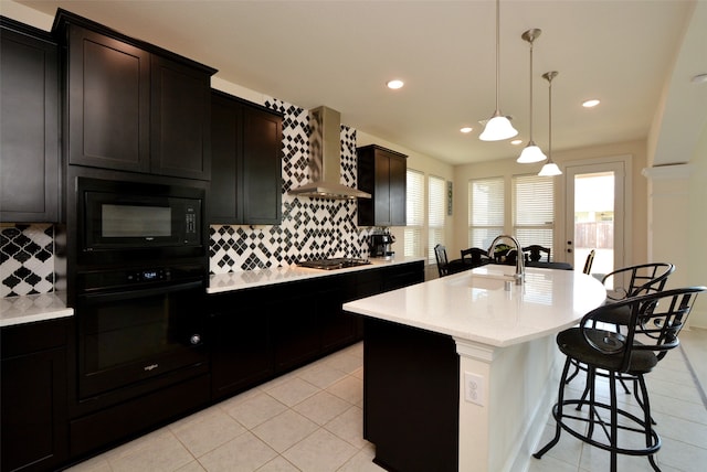 kitchen with tasteful backsplash, black appliances, a center island with sink, sink, and wall chimney range hood